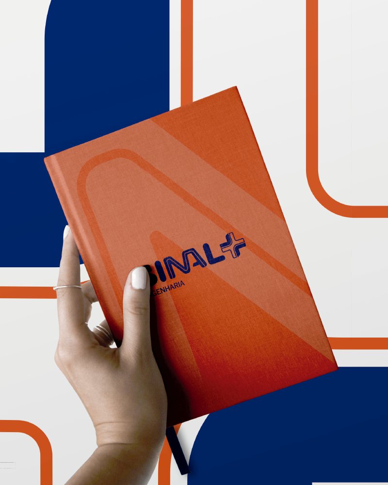 Caderno laranja com a marca Sinal Mais Engenharia